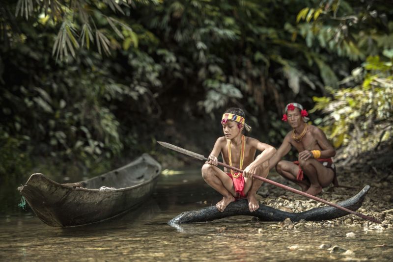 Native Indonesian tribe member boy at river with canoe