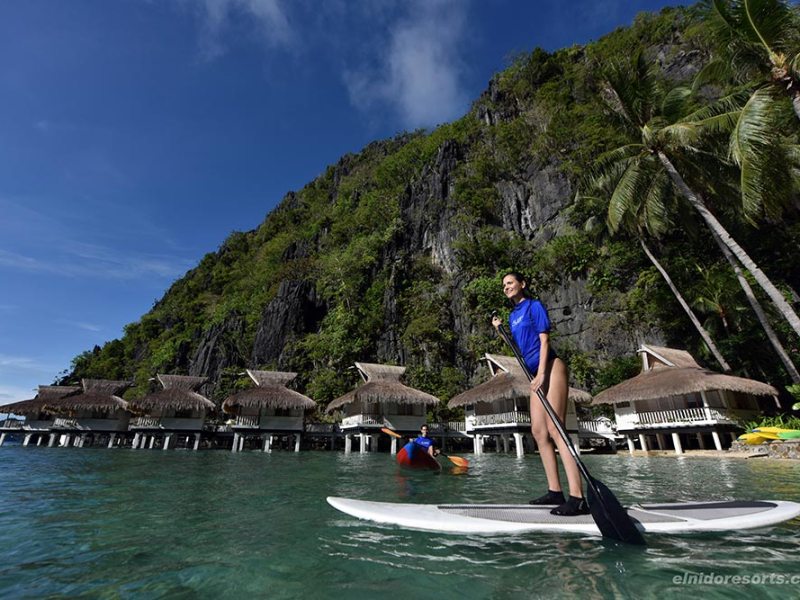 Woman stand up paddle boarding with water villas in background